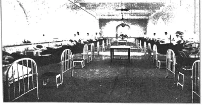 Photograph of a long hospital ward with rows of iron beds under a high arched ceiling with fans.