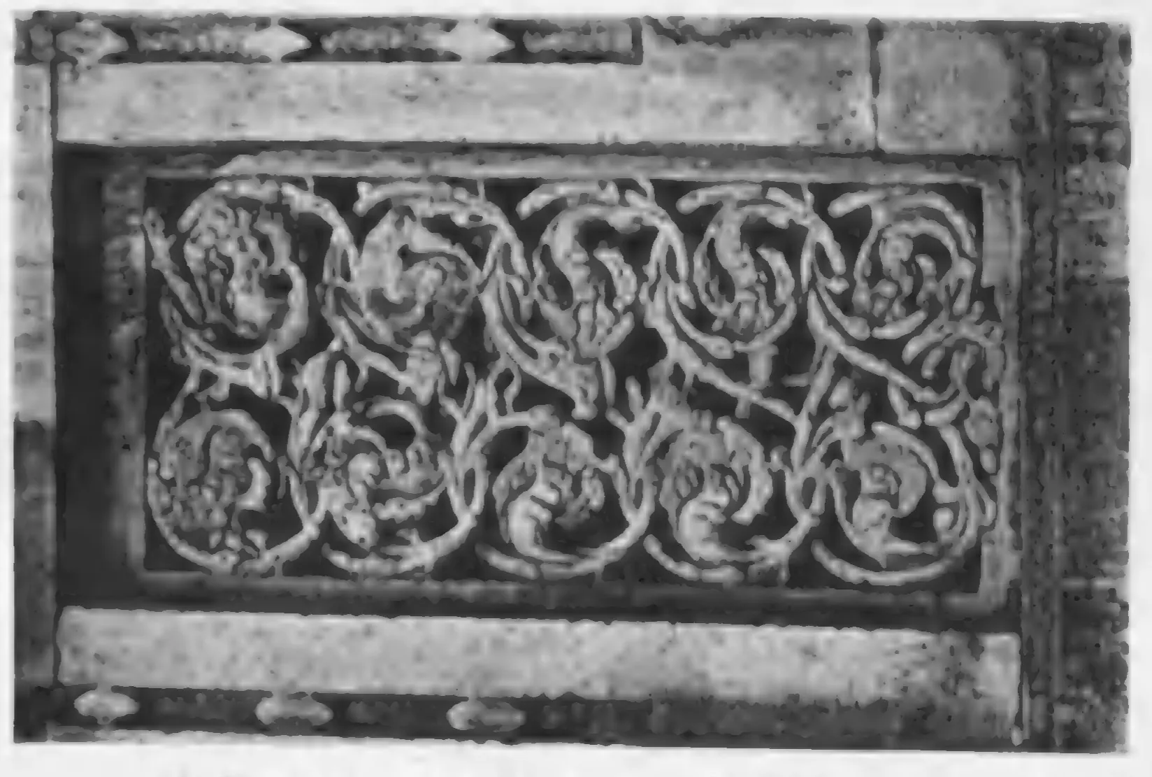 Old photograph of a pierced stone window screen with scrolling leaf and flower tracery, set in a carved frame.