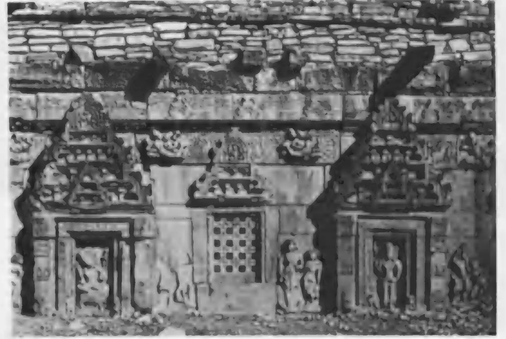 Old photograph of a temple wall with niches holding figure sculptures and a pierced stone window, above a moulded base.