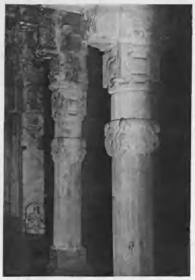 Old photograph of two tall stone pillars with cushion-shaped capitals inside a dark temple hall.