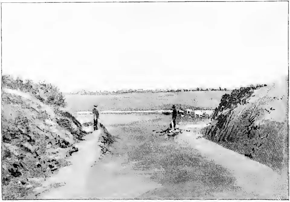 Faded old photograph of a broad sandy river bed between bushy banks, with water in the distance and two or three people standing on the sand.