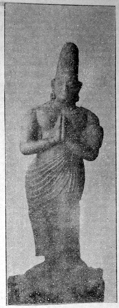 Faded photograph of a life-size stone statue of a standing man with a tall conical headdress, his hands joined in salutation, wearing a pleated lower garment.
