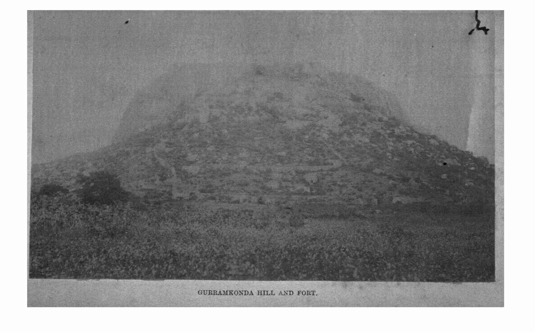 Faded photograph of a rocky hill with the fortifications of Gurramkonda along its slopes. Printed sideways.
