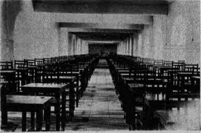 Photograph of a long vaulted basement hall with rows of wooden desks and benches on both sides of a central aisle.