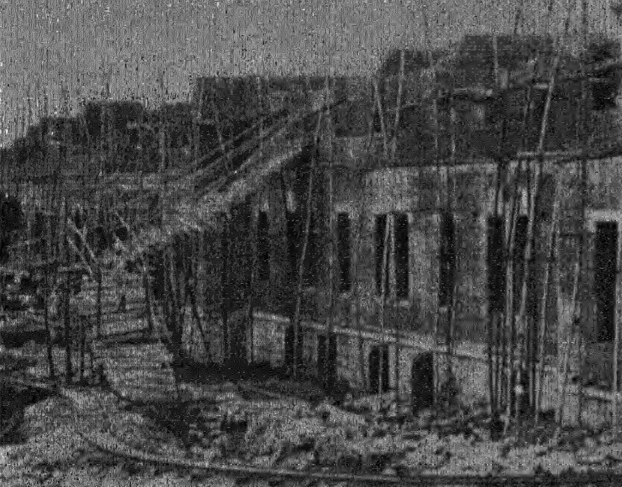 Photograph of a two-storeyed stone building with bamboo scaffolding along its walls and rough rock in the foreground.