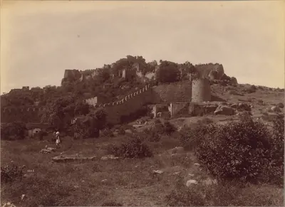 1887 sepia albumen photograph of Golconda Fort's ruined walls across a scrubby hillside, with two men standing near the fort.