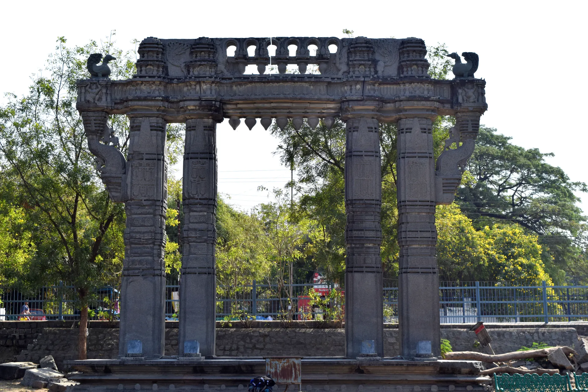 Frontal view of a Kakatiya Kala Thoranam, a stone gateway at Warangal Fort with four carved pillars, a heavy lintel and hamsa birds on top.