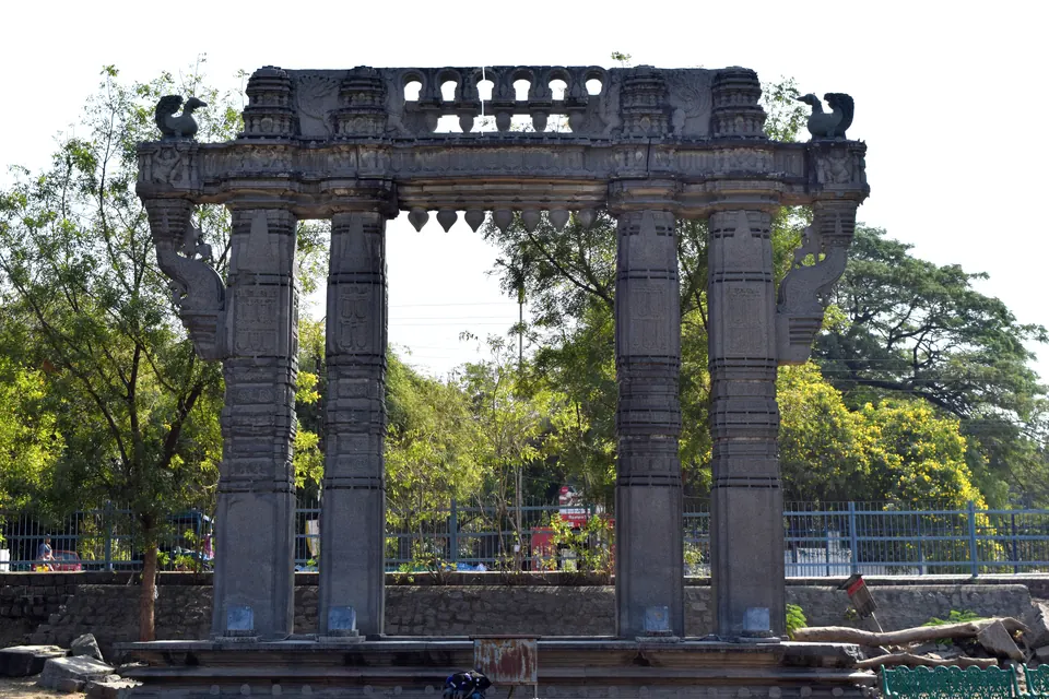 Frontal view of a Kakatiya Kala Thoranam, a stone gateway at Warangal Fort with four carved pillars, a heavy lintel and hamsa birds on top.