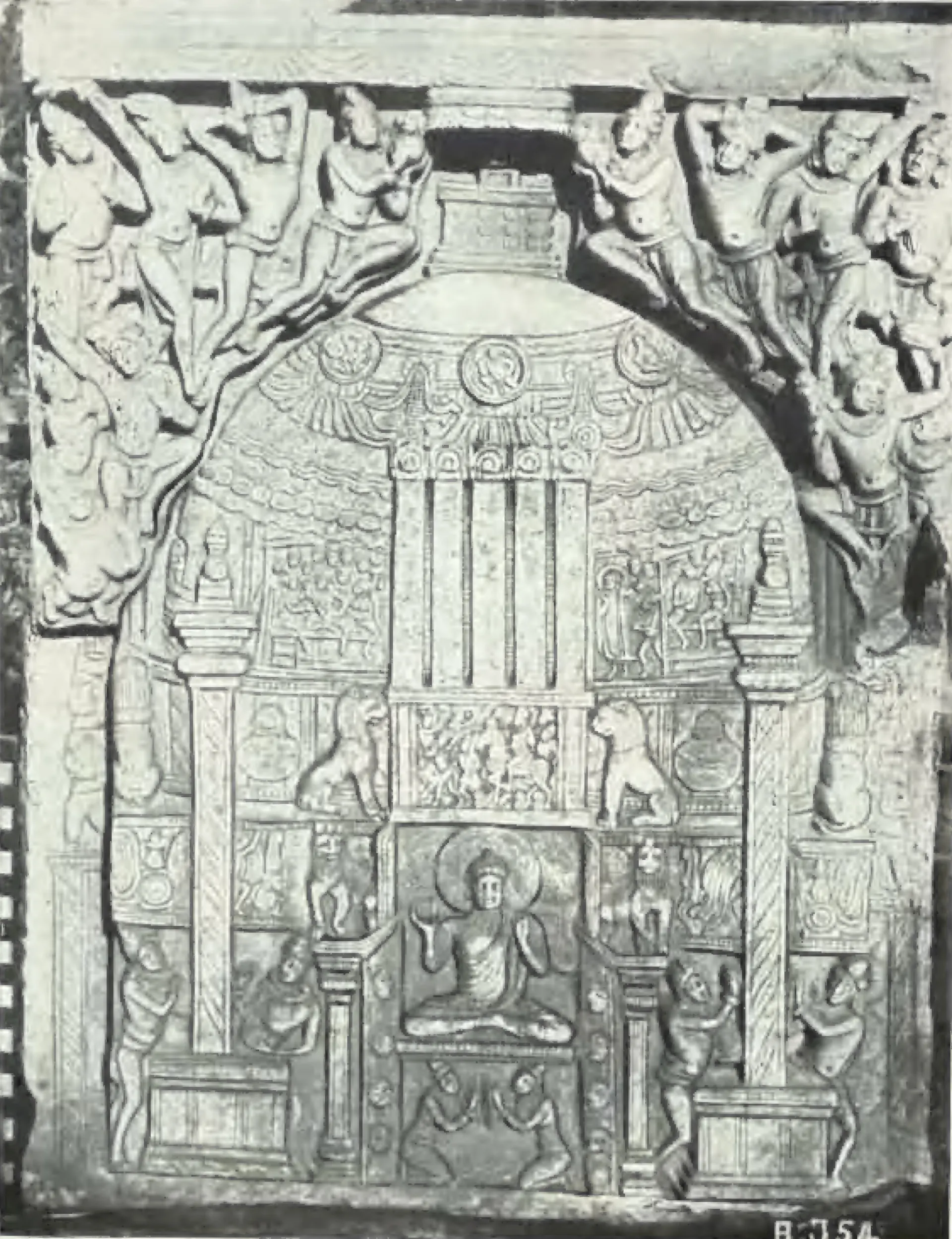 A carved limestone relief of a stupa under an arch, with a seated Buddha at its base, pillars and lions at the sides and flying figures above.
