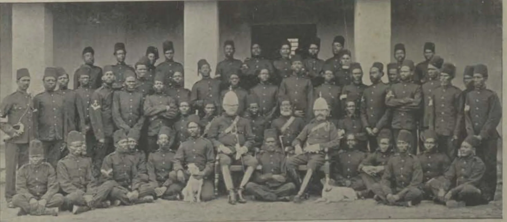 A large group of the Nizam's African guards in uniform, seated and standing in front of a building.