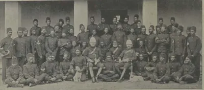 A large group of the Nizam's African guards in uniform, seated and standing in front of a building.