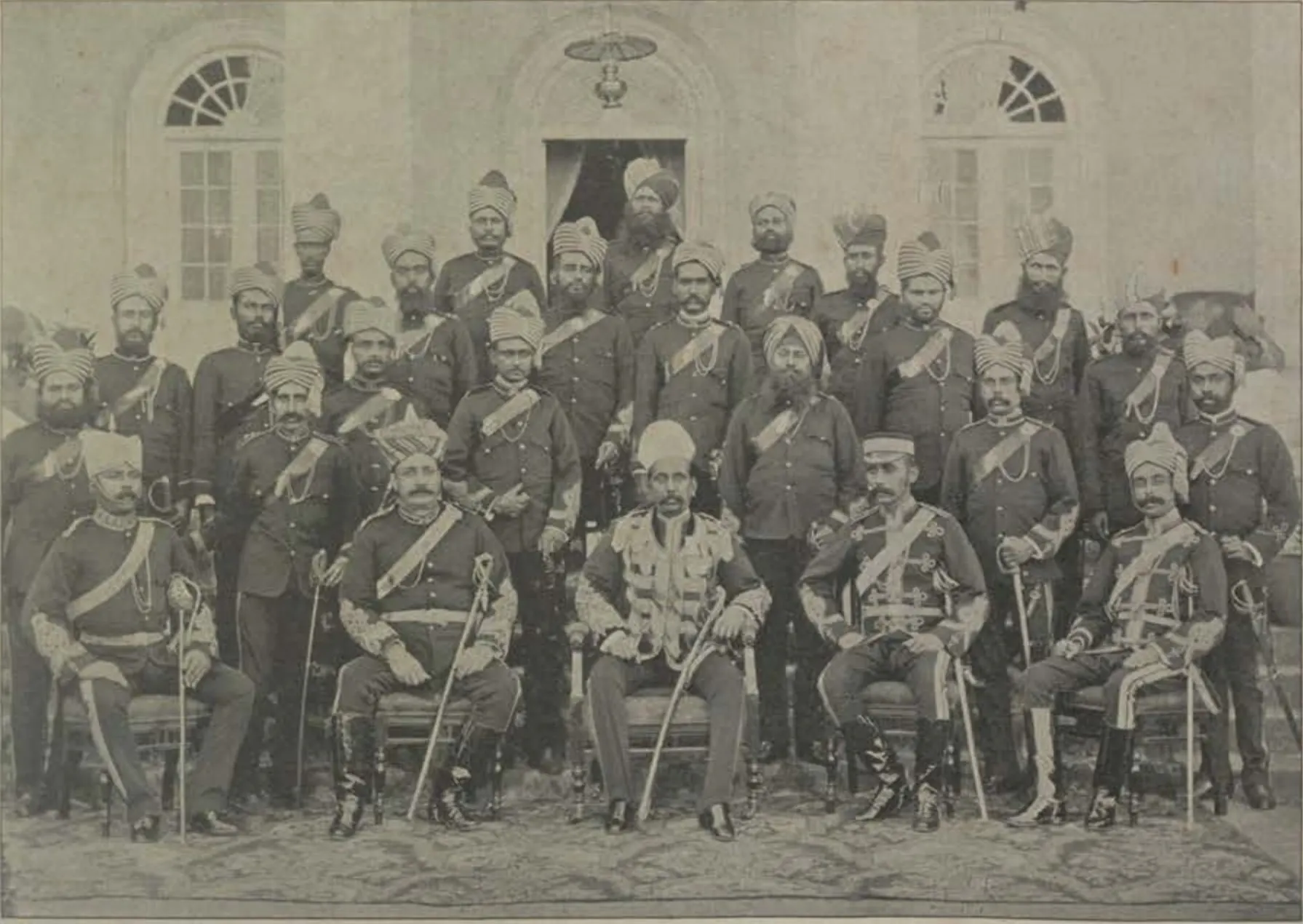 The City Kotwal and his police officers in uniform, seated and standing in front of a building.