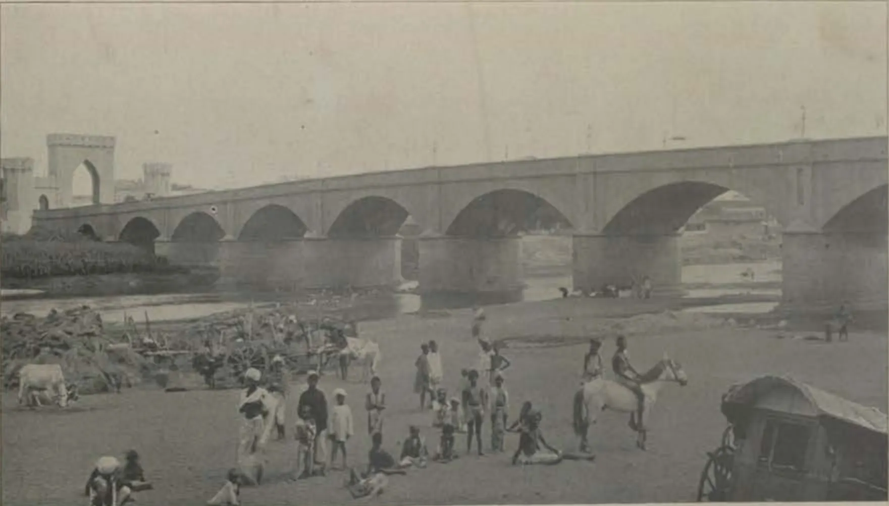 The Afzal bridge, with its row of arches, over the Musi river, with people in the river bed.