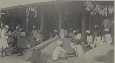 Traders seated beside heaps of grain under a roofed market.