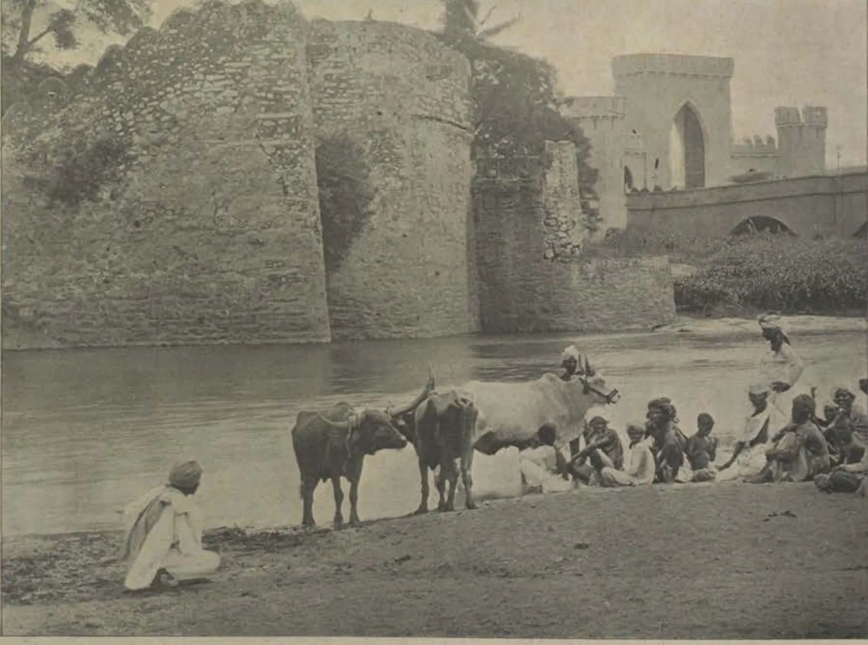 A river bank with men and cattle, and ruined walls and a gateway beyond.
