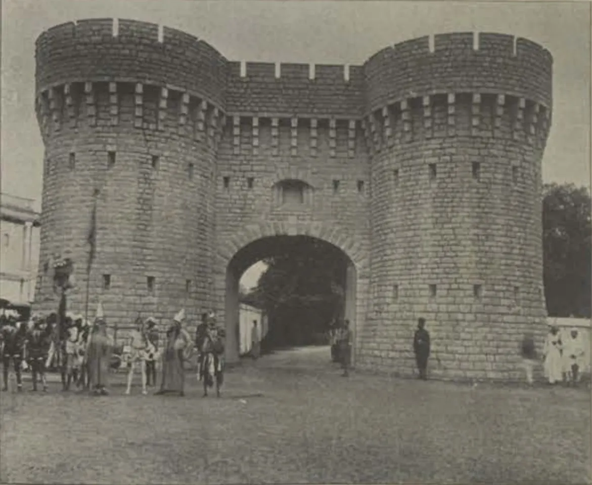 The Residency gate, a castellated gateway between two round towers, with people in front.
