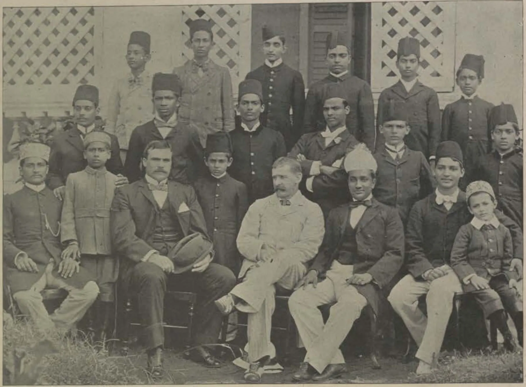 A large group of teachers and students of the Nizam College, seated and standing in rows in front of a building with lattice windows.