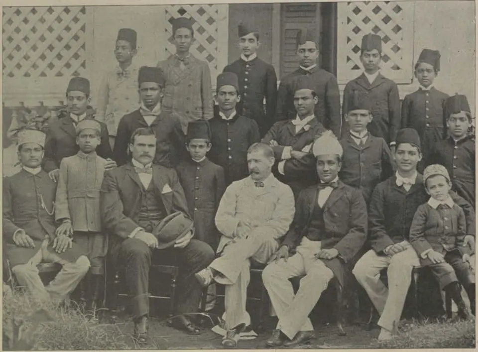 A large group of teachers and students of the Nizam College, seated and standing in rows in front of a building with lattice windows.
