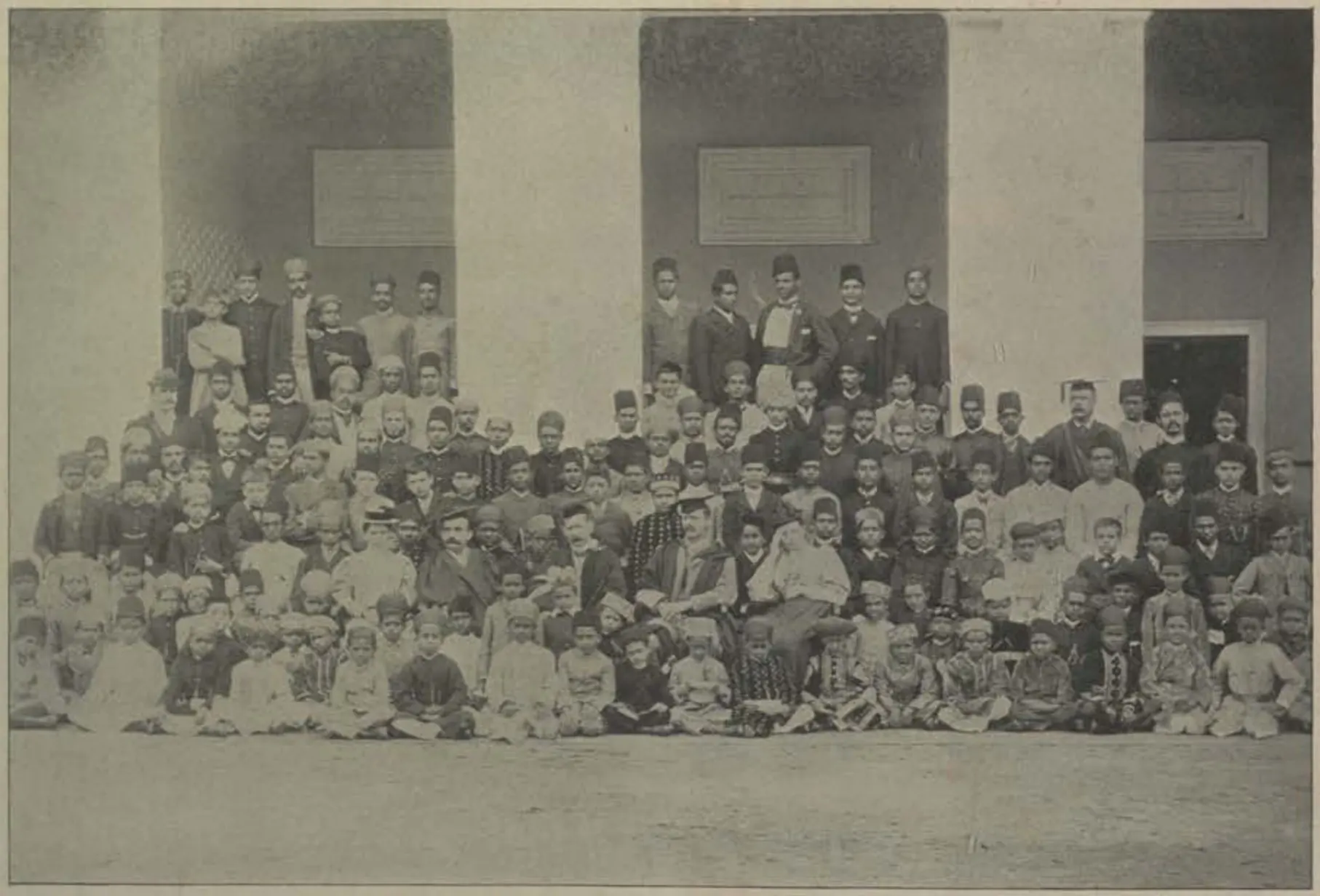 A large group of students of the Madrasa-i-Aliya seated in rows in front of a building.