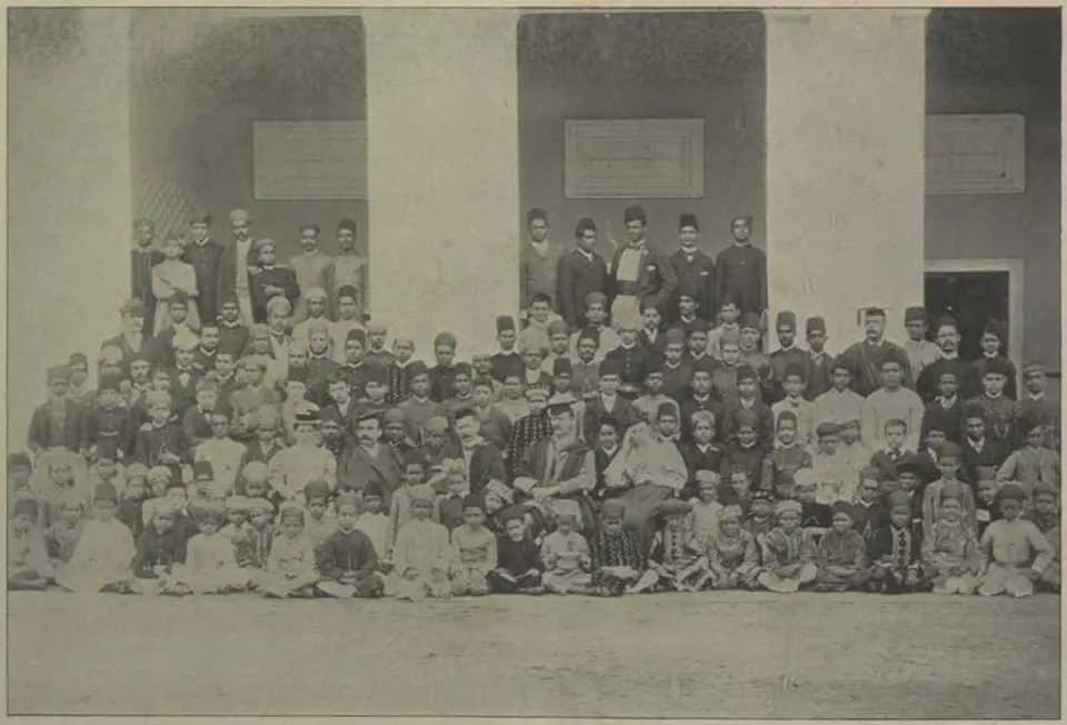 A large group of students of the Madrasa-i-Aliya seated in rows in front of a building.