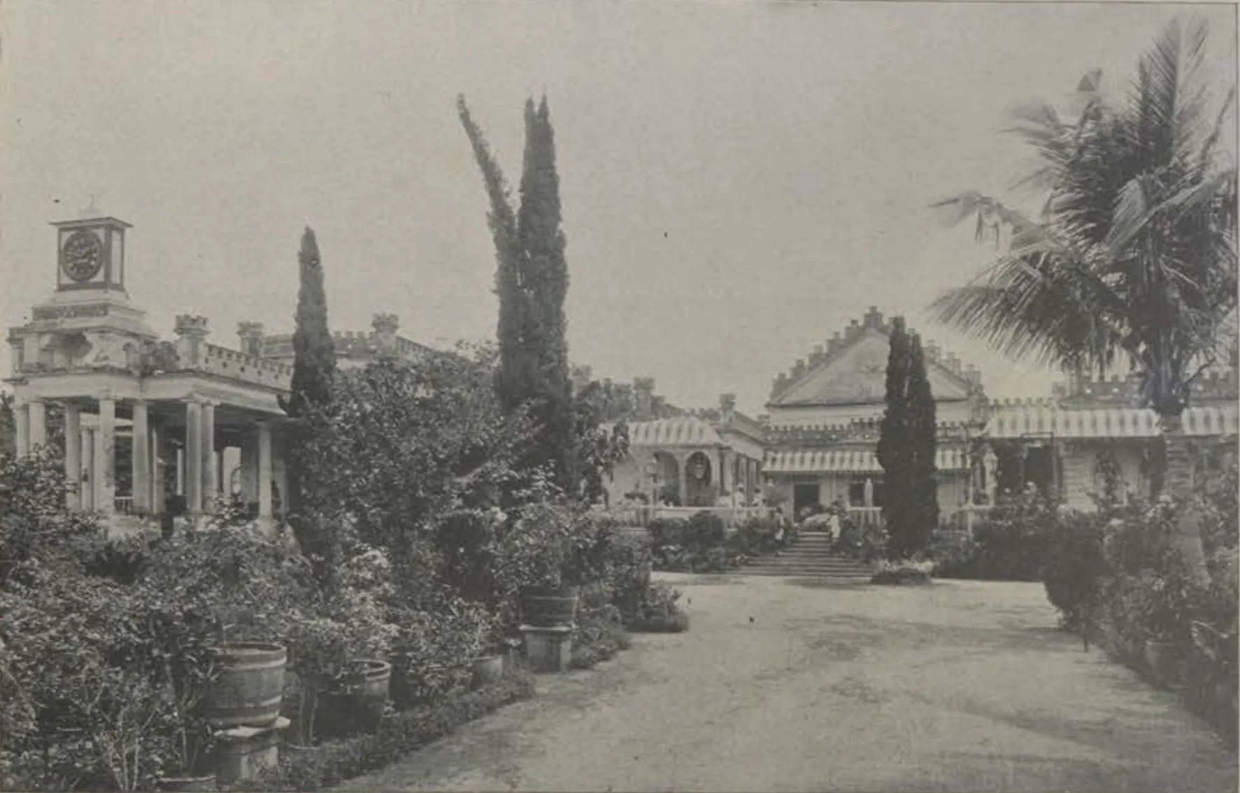 Shapur Wadi, buildings along a garden path with palms and cypresses.