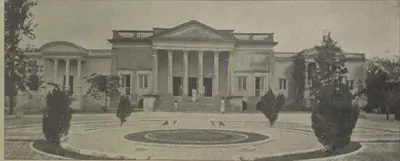 A classical building with a portico behind a circular lawn.