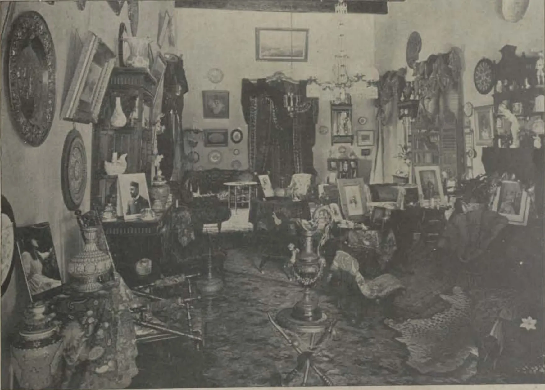 A drawing room crowded with pictures, ornaments and furniture.