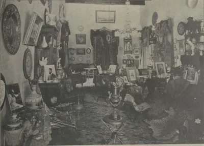 A drawing room crowded with pictures, ornaments and furniture.