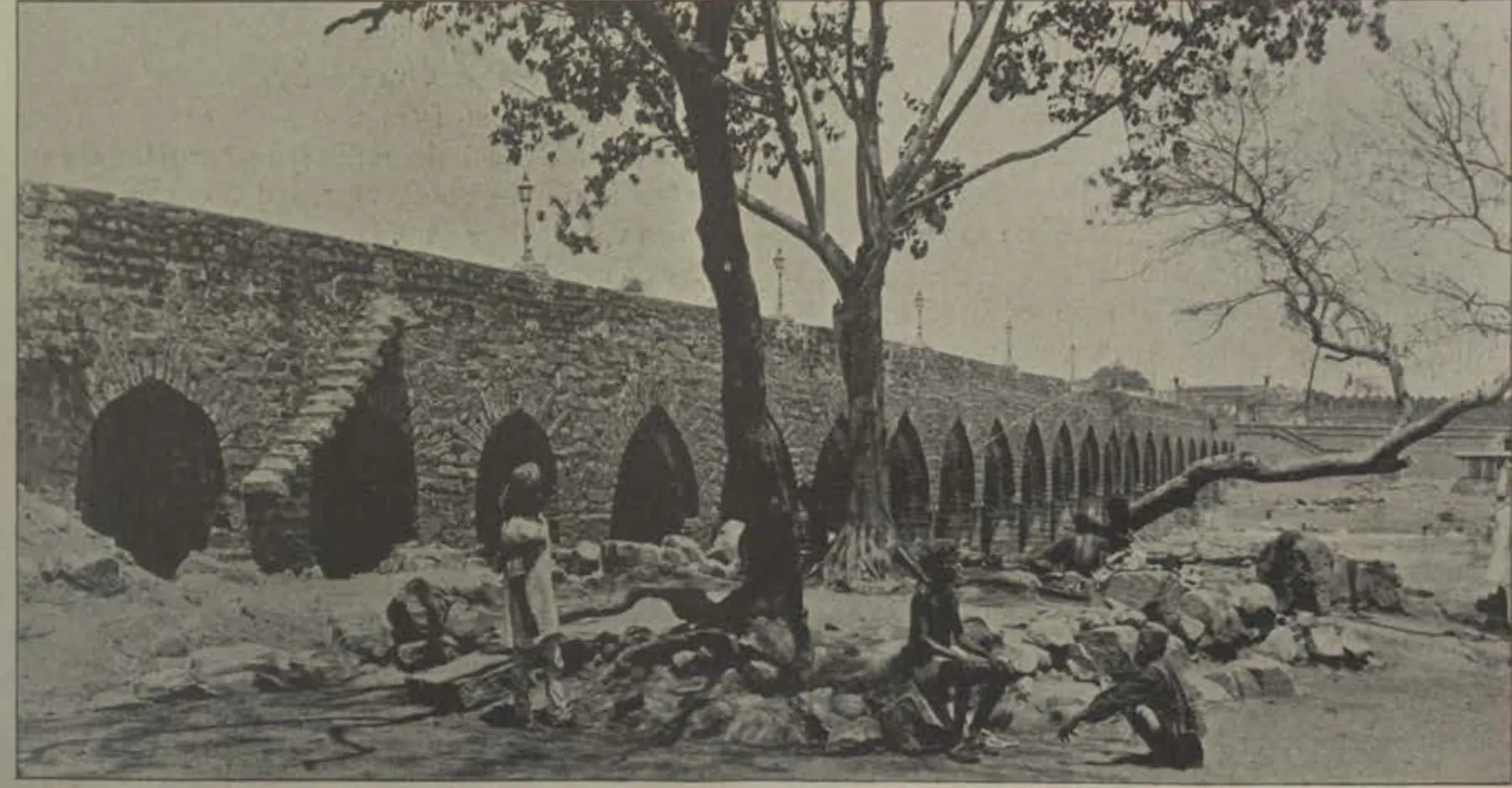 The old bridge, with its many arches, with trees and people in front.