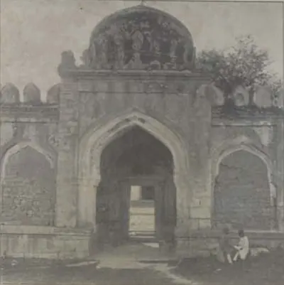 An arched gateway with a dome above it, with men seated in front.