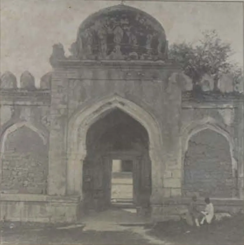 An arched gateway with a dome above it, with men seated in front.