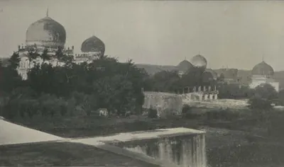 Several domed tombs among trees, inside an enclosure wall.