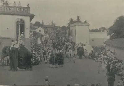 An elephant carrying a standard-bearer in a crowded street procession.