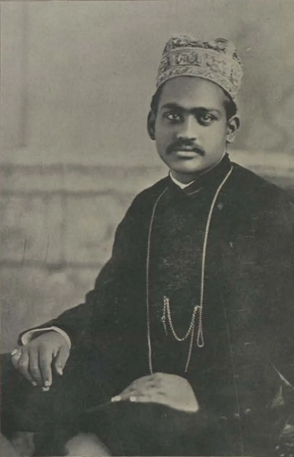 Raja Ramasor Row II seated, in an embroidered cap and dark coat with a watch chain.