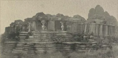The stepped stone platform of a ruined temple with pillars on top and a rocky hill behind.