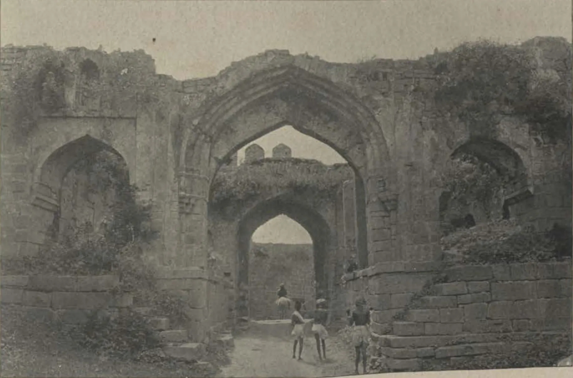 The Hyderabad Gate of Warangal, a ruined arched gateway, with people in the passage.