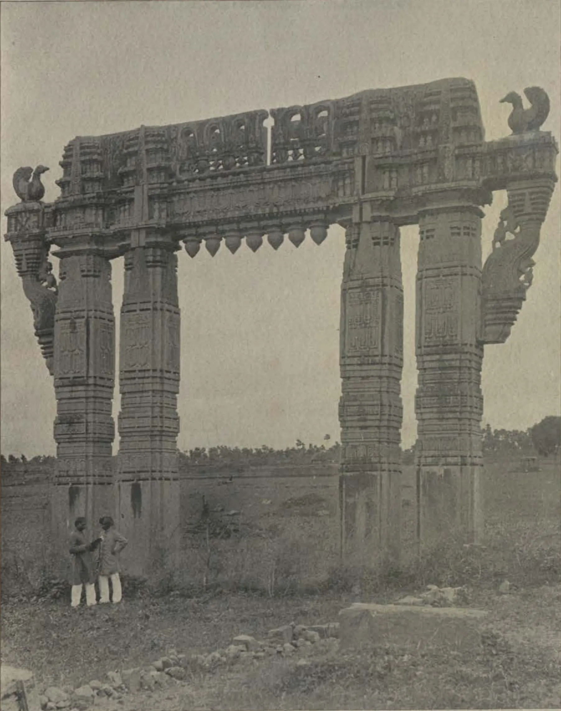 A carved stone gateway (torana) of Warangal fort standing in open ground, with people beneath it.