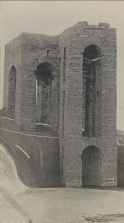 A tall ruined masonry structure with arched openings, beside a well on the summit.