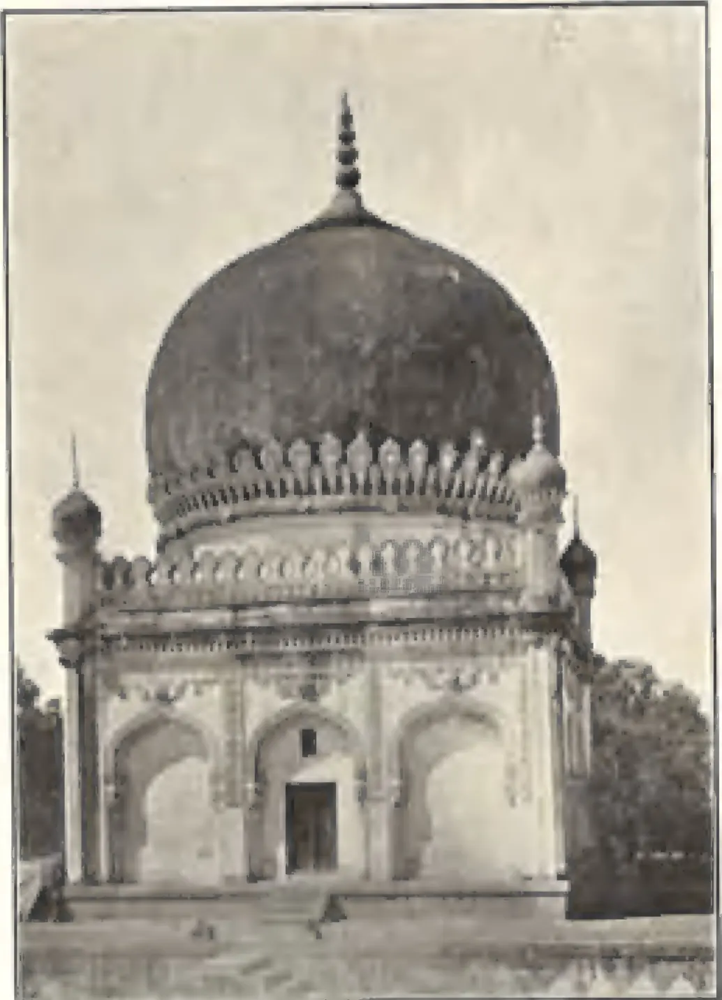 A domed building near the gate of the Golconda tombs, with a dark bulbous dome and arched walls.