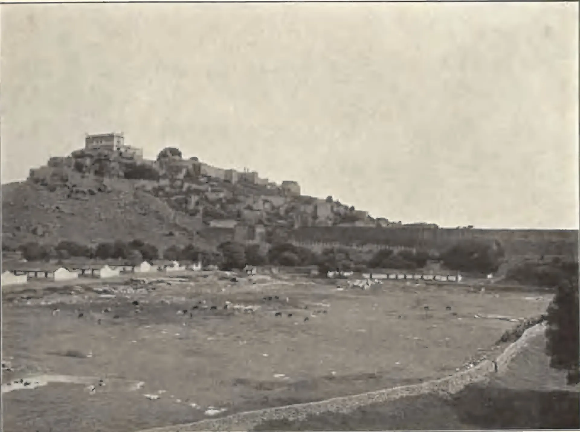 General view of Golconda fort on its rocky hill, with houses and an open plain in front.