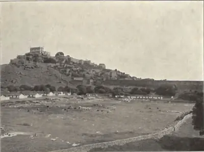 General view of Golconda fort on its rocky hill, with houses and an open plain in front.