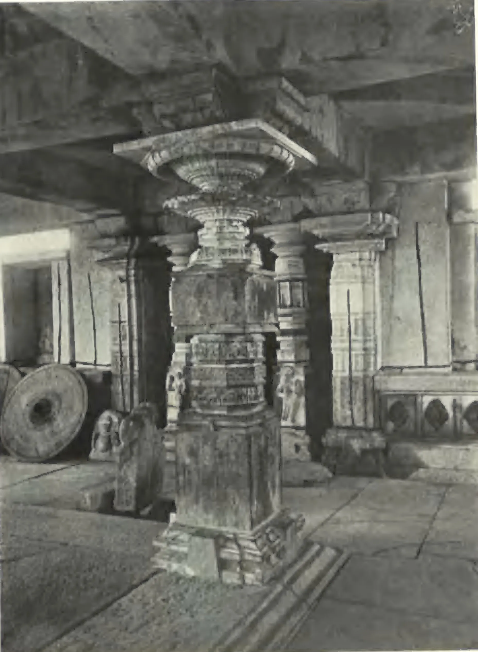 A carved pillar inside the Panchesvara temple at Panagal, with a millstone lying beside it.