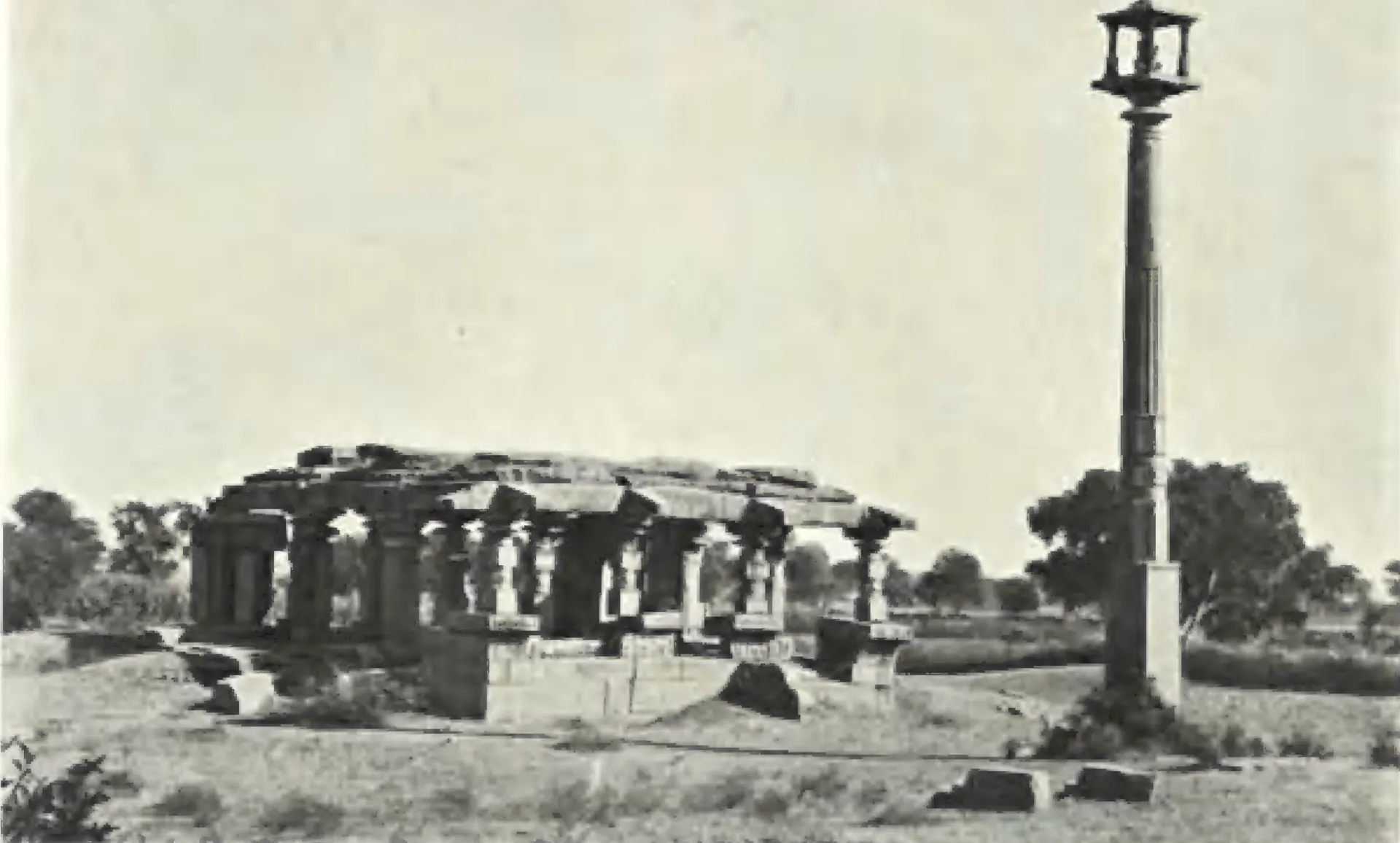 A ruined Vishnu temple at Nagunur with a pillared hall and a tall lamp pillar beside it.
