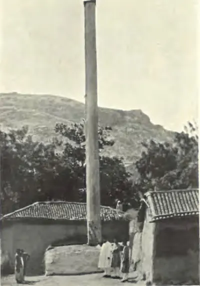 A tall monolithic stone pillar standing among houses at Nalgonda, with a hill behind.