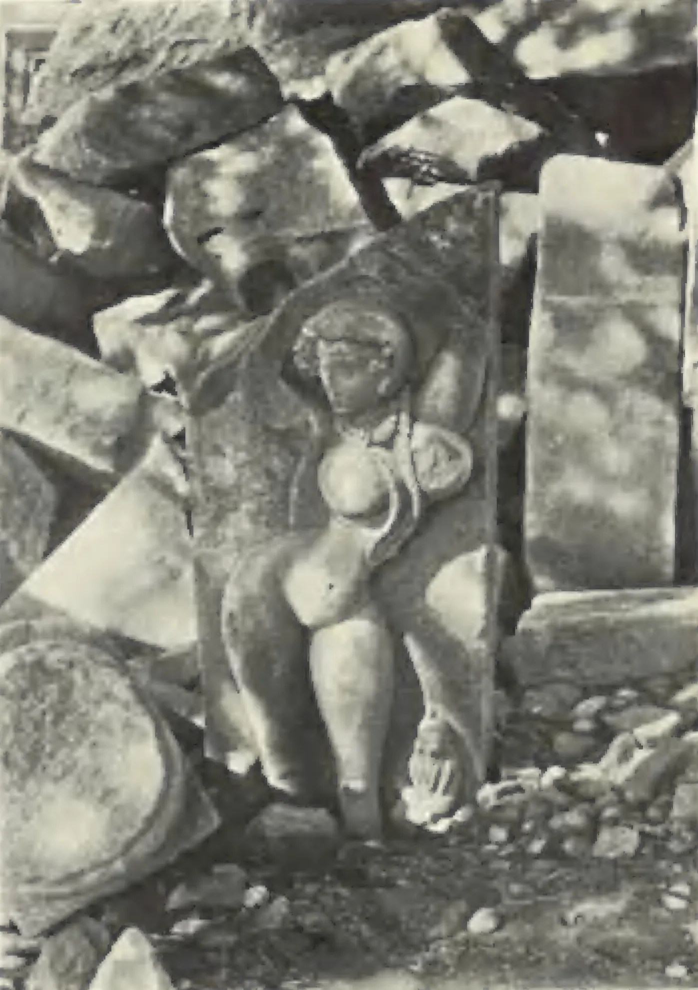 A carved figure on a fallen stone slab among broken stones at Pedampet.