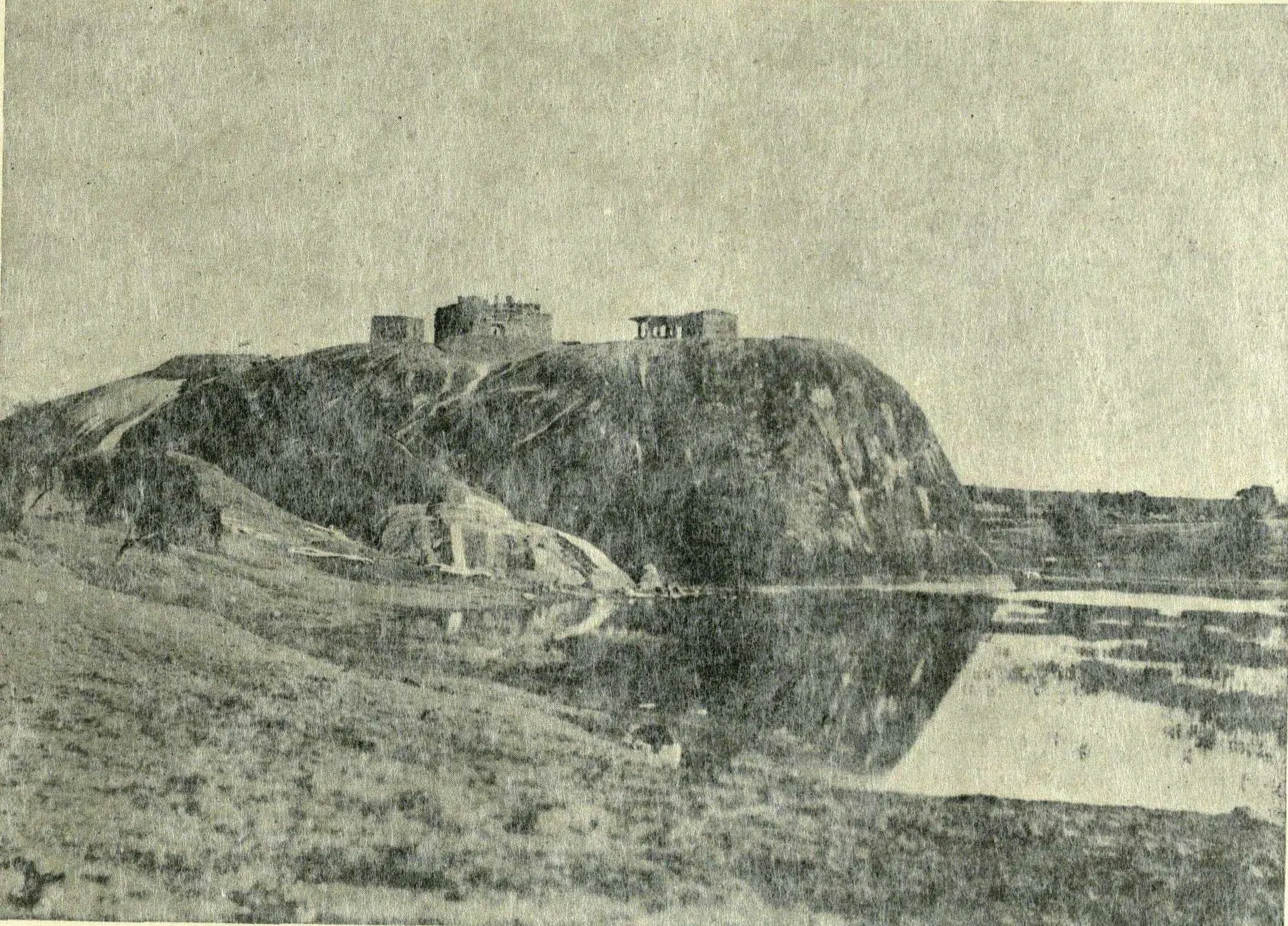 The rock of Warangal fort with ruins on top, reflected in water in front.