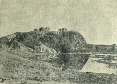 The rock of Warangal fort with ruins on top, reflected in water in front.
