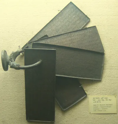 Five dark copper plates fanned out on a wall, held by a heavy ring that ends in a round seal at the left; a museum label at the lower right reads "Amma II (Eastern Chalukya), Script: Canarese-Telugu, Language: Sanskrit, 10th century A.D."