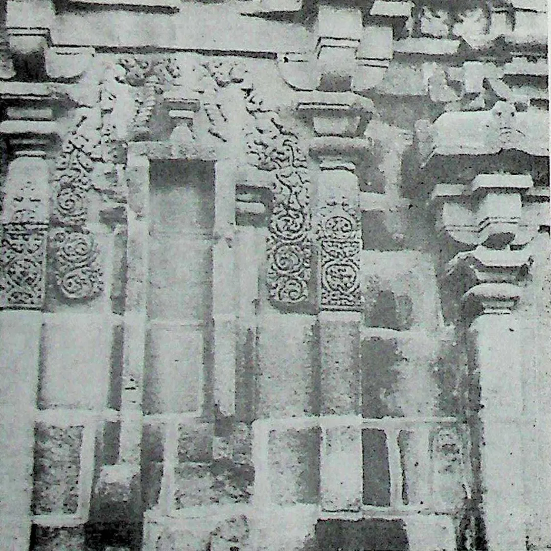 The back wall of a stone temple: pilasters, a tall central niche and panels of carved scrollwork under a cornice of small roof-shaped mouldings.