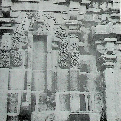 The back wall of a stone temple: pilasters, a tall central niche and panels of carved scrollwork under a cornice of small roof-shaped mouldings.